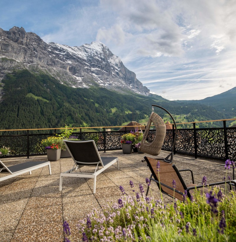 Mountain-view terrace with vibrant flower pots and loungers, evoking serenity perfect for vacation retreats.