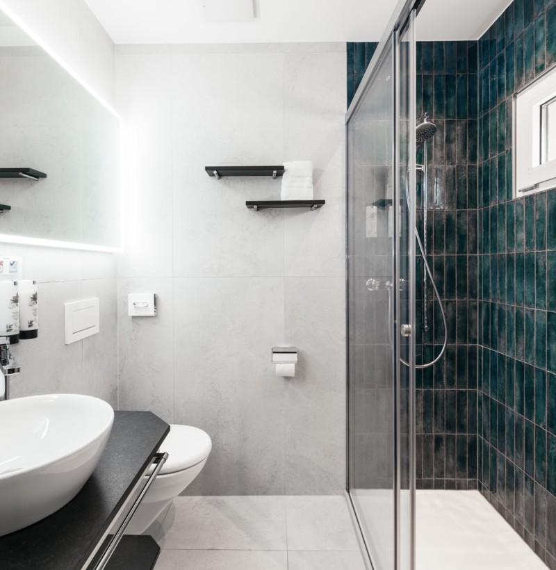 Sleek bathroom with white fixtures and deep teal tiles, offering a clean, modern aesthetic for design-focused homeowners.
