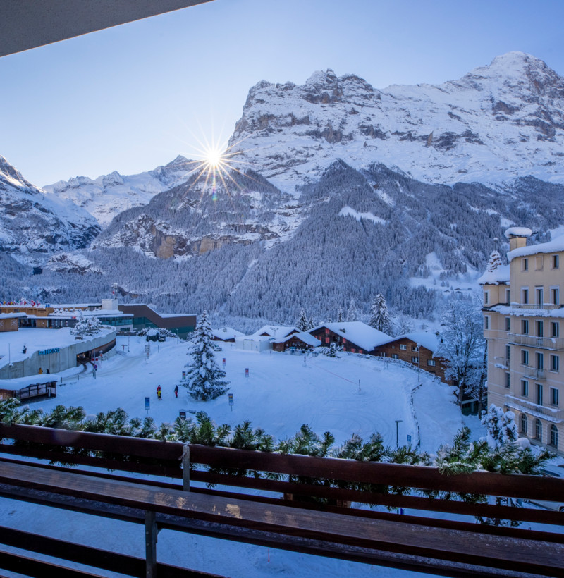 Winter sunrise over a snow-covered mountain village, viewed from a balcony, evoking a serene and picturesque getaway for travelers.