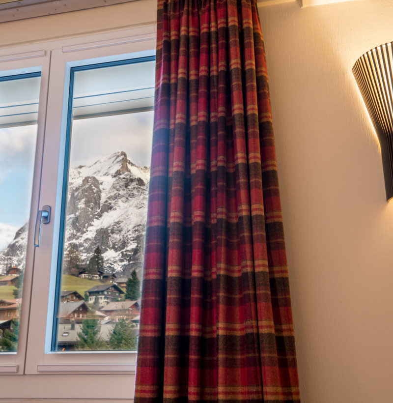 Cozy room with a plaid curtain and modern wall sconce, framing a snowy mountain view, evoking a warm, serene ambiance ideal for relaxation.