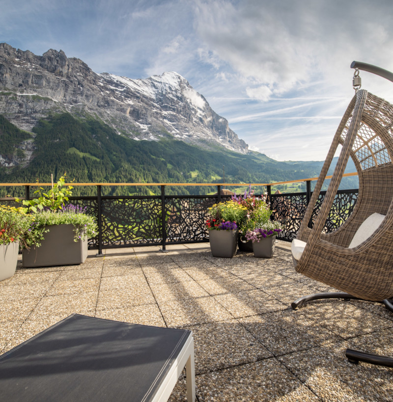 Alpine balcony with a wicker egg chair and vibrant flowerpots, evoking serene luxury, ideal for travel and leisure sectors.