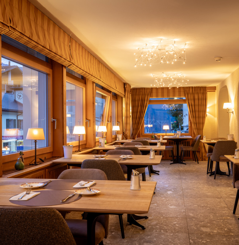Warmly lit restaurant with wooden furnishings and modern lighting, creating a cozy ambiance for dining experiences.