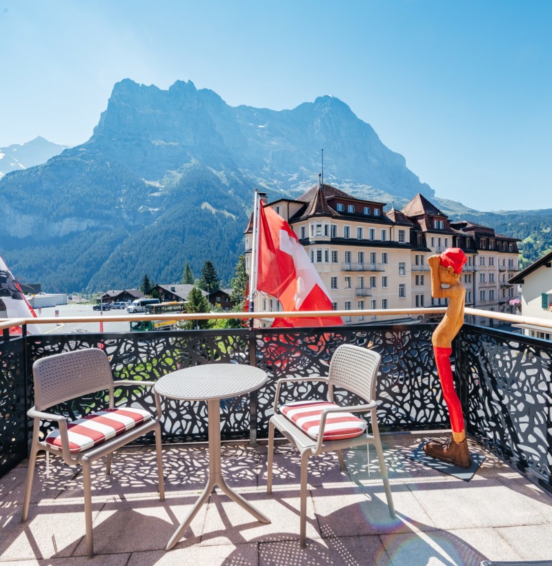 Bright, welcoming outdoor patio with Swiss flags under the majestic Alps, ideal for travel and leisure marketing.