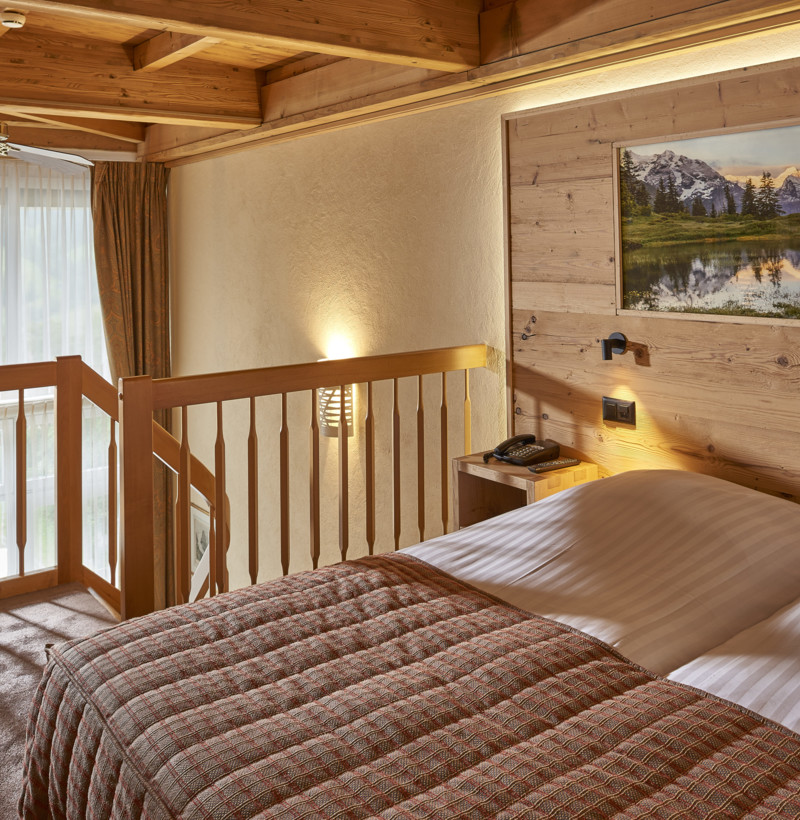 Cozy wooden cabin bedroom with plaid bedding and serene mountain artwork, evoking a tranquil, rustic retreat vibe ideal for relaxation.