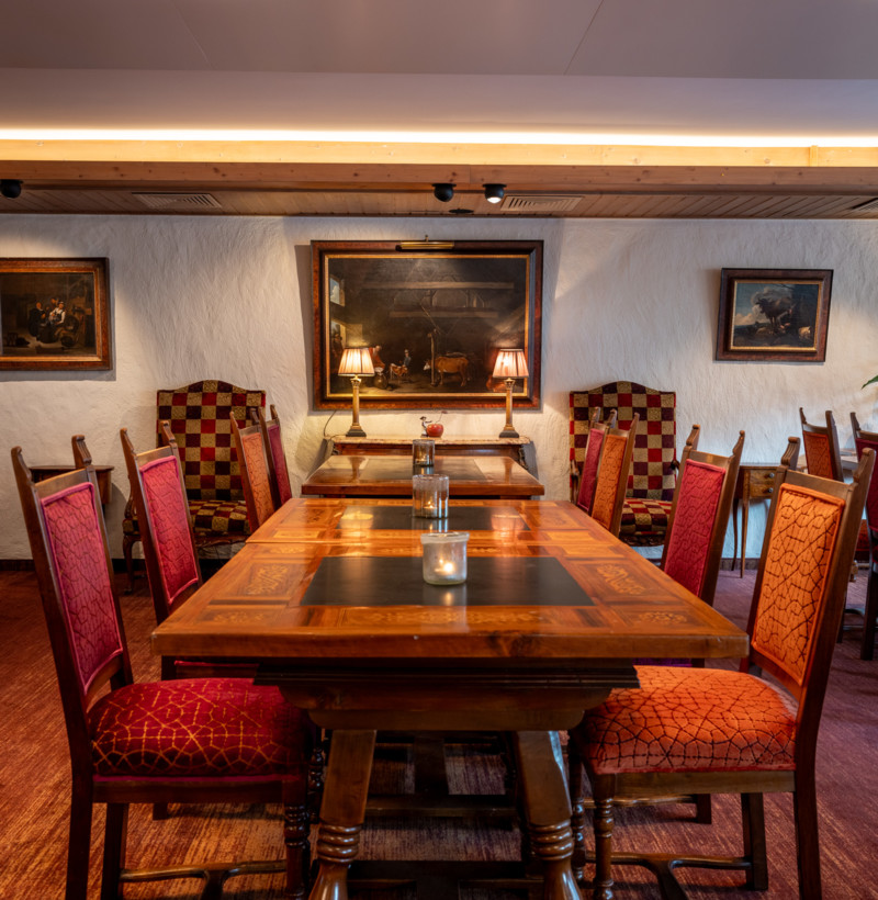 Elegant dining setup with polished wooden tables and red patterned chairs, highlighted by circular overhead lights, exuding a warm, inviting ambiance for diners.