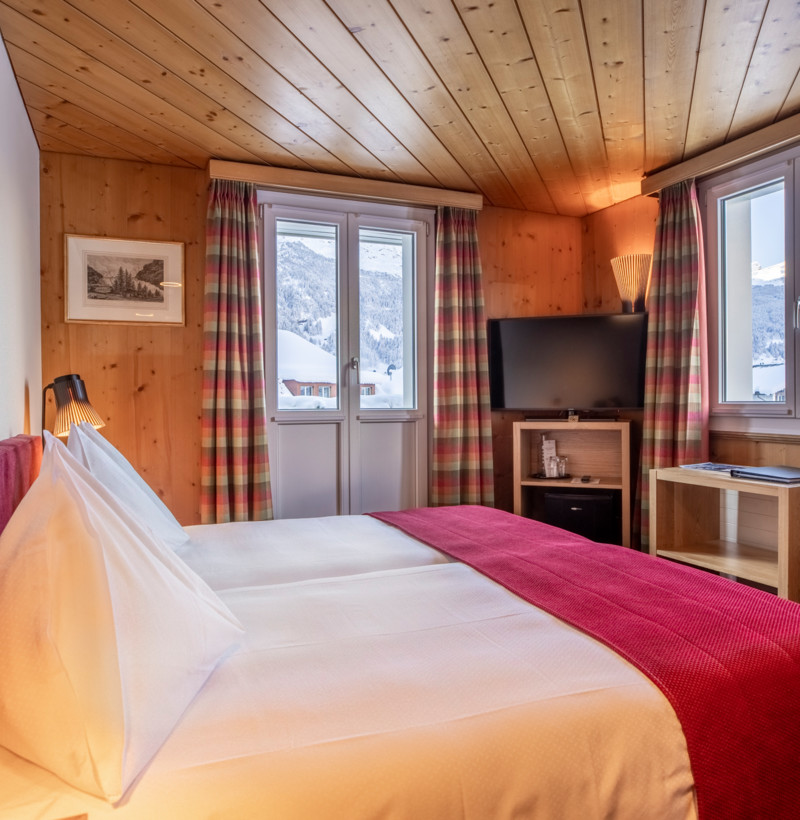 Cozy alpine hotel room with warm wooden interiors and red accents, offering a serene and inviting mountain getaway.