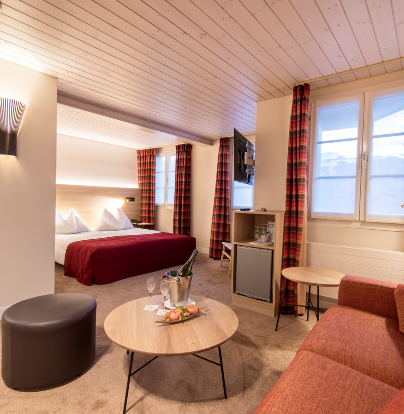 Cozy hotel room with a rich red bed, tartan curtains, and soft lighting, offering a warm, inviting atmosphere for travelers.