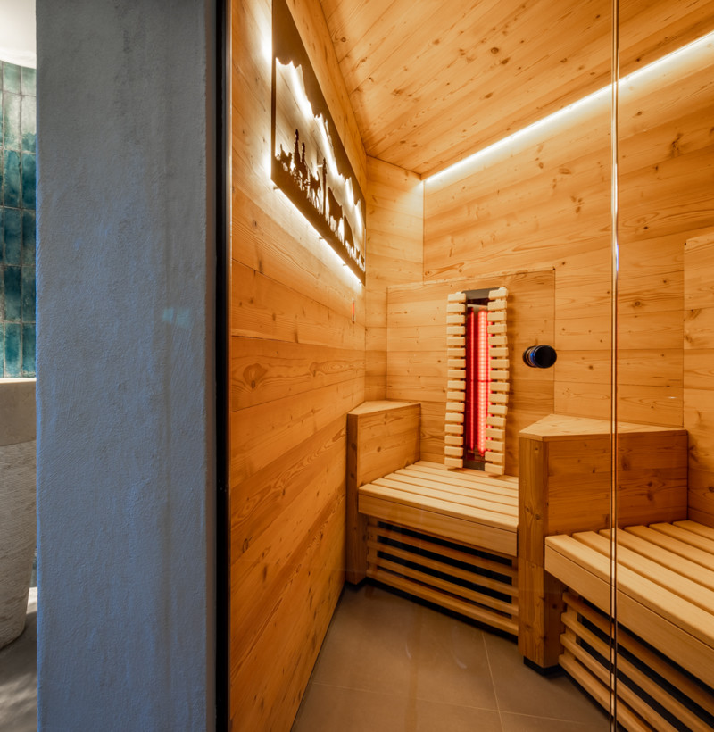 Warm wooden sauna with glowing red heaters and serene blue bathroom tiles, providing an inviting and restful ambiance for wellness spaces.