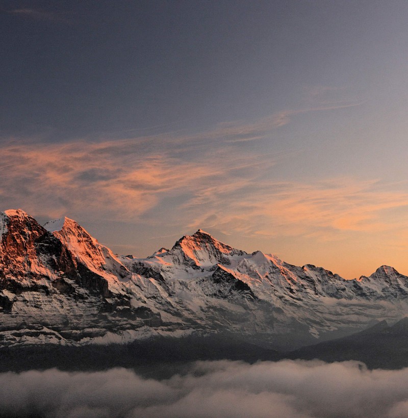 Majestic snow-capped peaks bathed in warm sunset hues, evoking serenity for outdoor and travel enthusiasts.