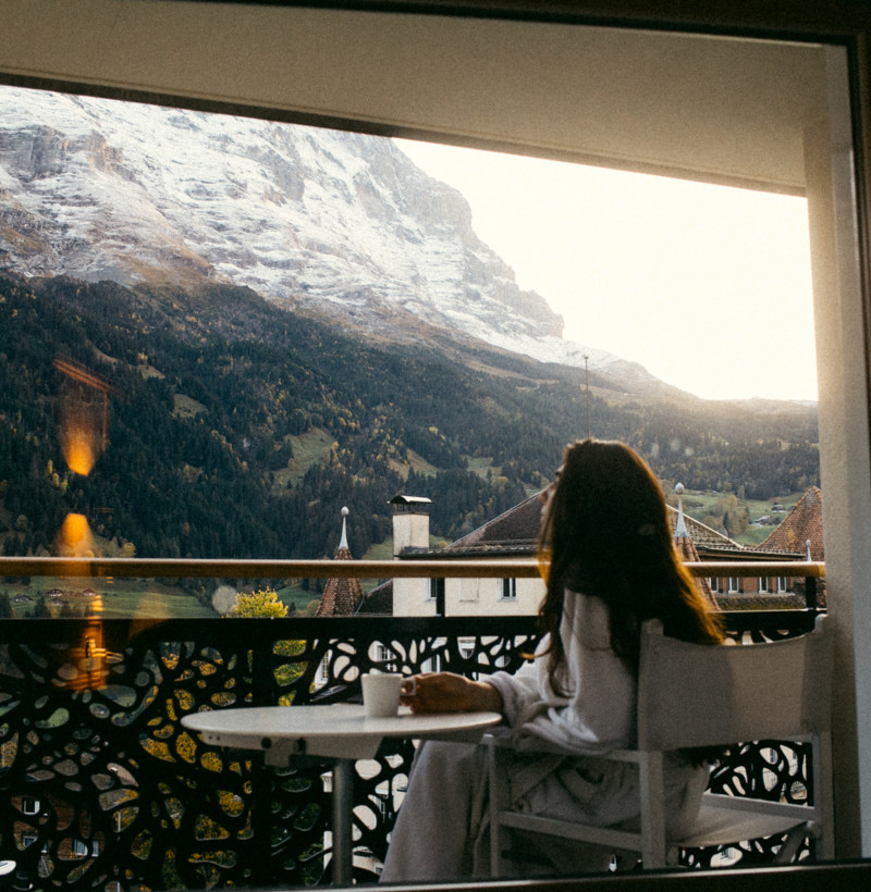Woman enjoys a serene morning view of snowy mountains from a balcony, evoking peace and relaxation, ideal for travel and leisure sectors.