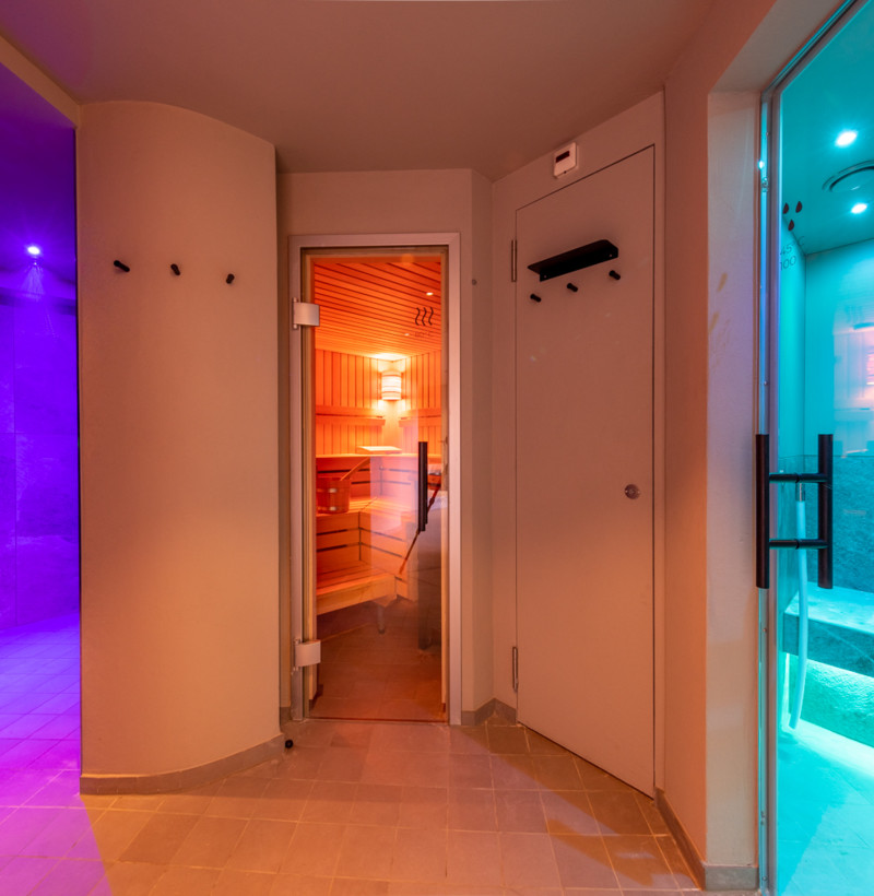 Mood-lit spa corridor featuring warm wooden sauna and cool blue-lit pool, inviting relaxation in a luxury wellness center.