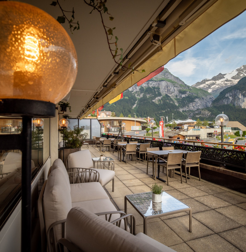 Alpine terrace café with cozy seating and panoramic mountain views, inviting relaxation in a vibrant tourism hub.