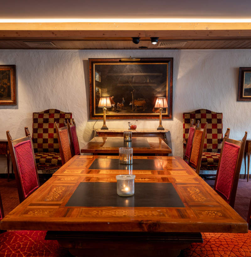 A warmly lit dining room with rich wooden tables and plush red chairs, creating a cozy, inviting atmosphere for restaurant patrons.