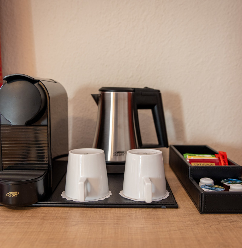 Cozy coffee corner with an espresso machine, kettle, and tea selection, set against a vibrant red and gold curtain, creating a welcoming vibe for beverage lovers.