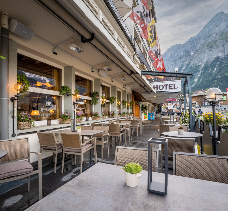 Charming outdoor café with beige furniture and lush potted plants, nestled in a picturesque mountain town, exuding a relaxed and inviting atmosphere.