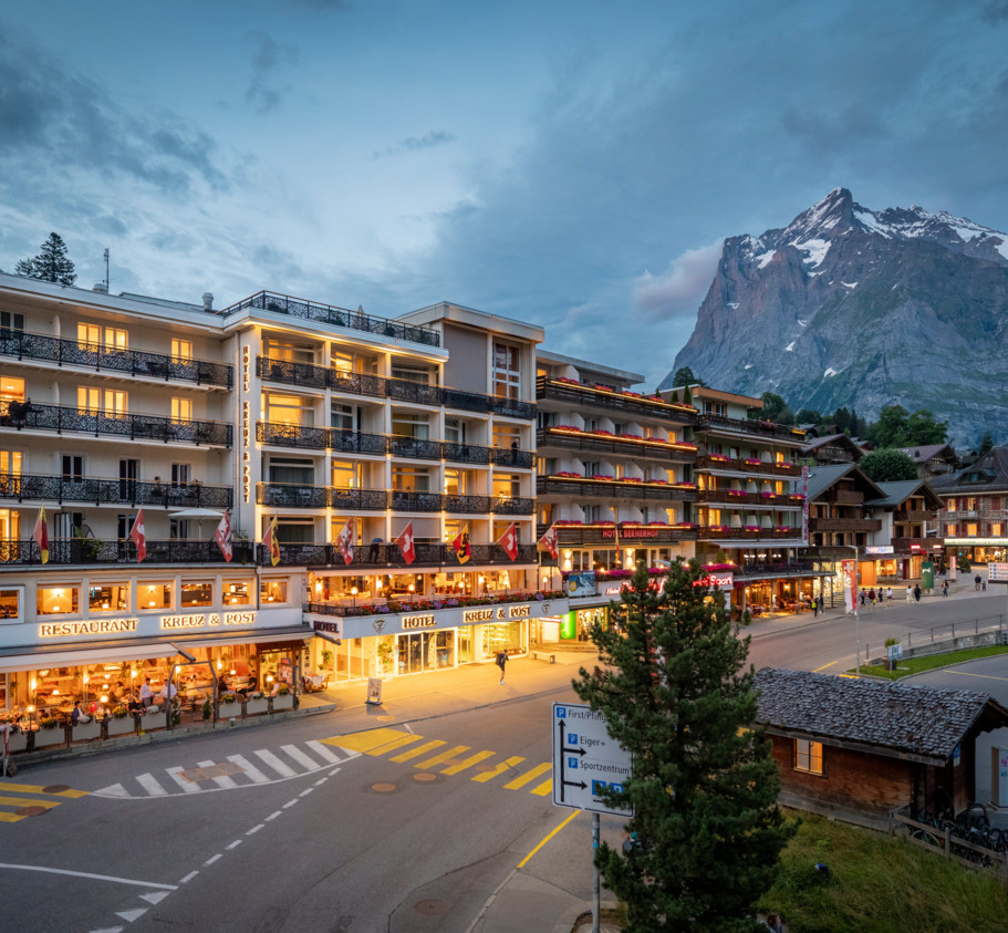 Twilight over a bustling hotel with lit balconies, nestled against a dramatic mountain backdrop, evokes a sense of adventurous escape in a tourist haven.
