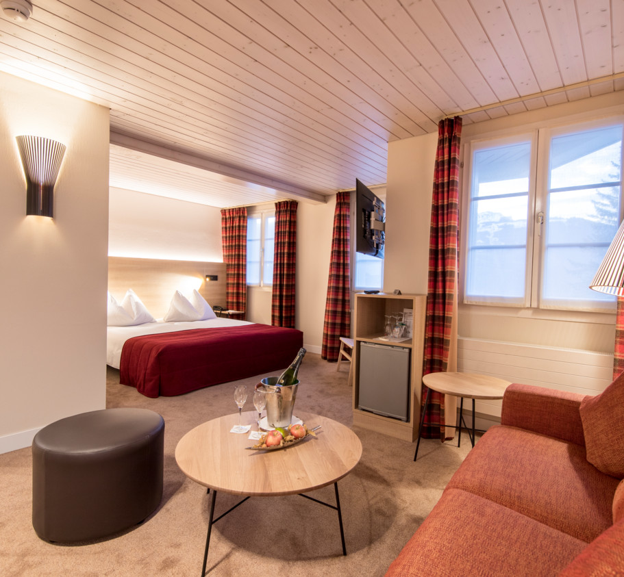 Cozy hotel room with a rich red bed, tartan curtains, and soft lighting, offering a warm, inviting atmosphere for travelers.