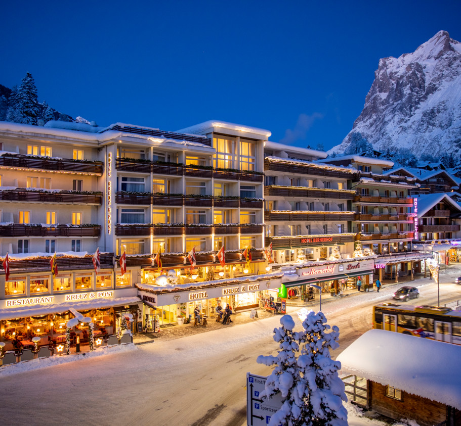 Twilight illuminates a snow-covered hotel with warm, glowing lights, creating a cozy, inviting atmosphere for winter travelers.